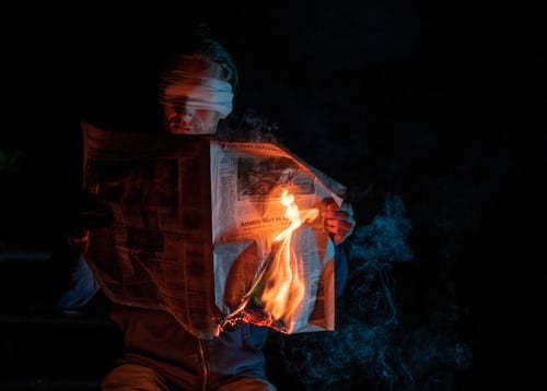 blindfolded man with newspaper on fire
