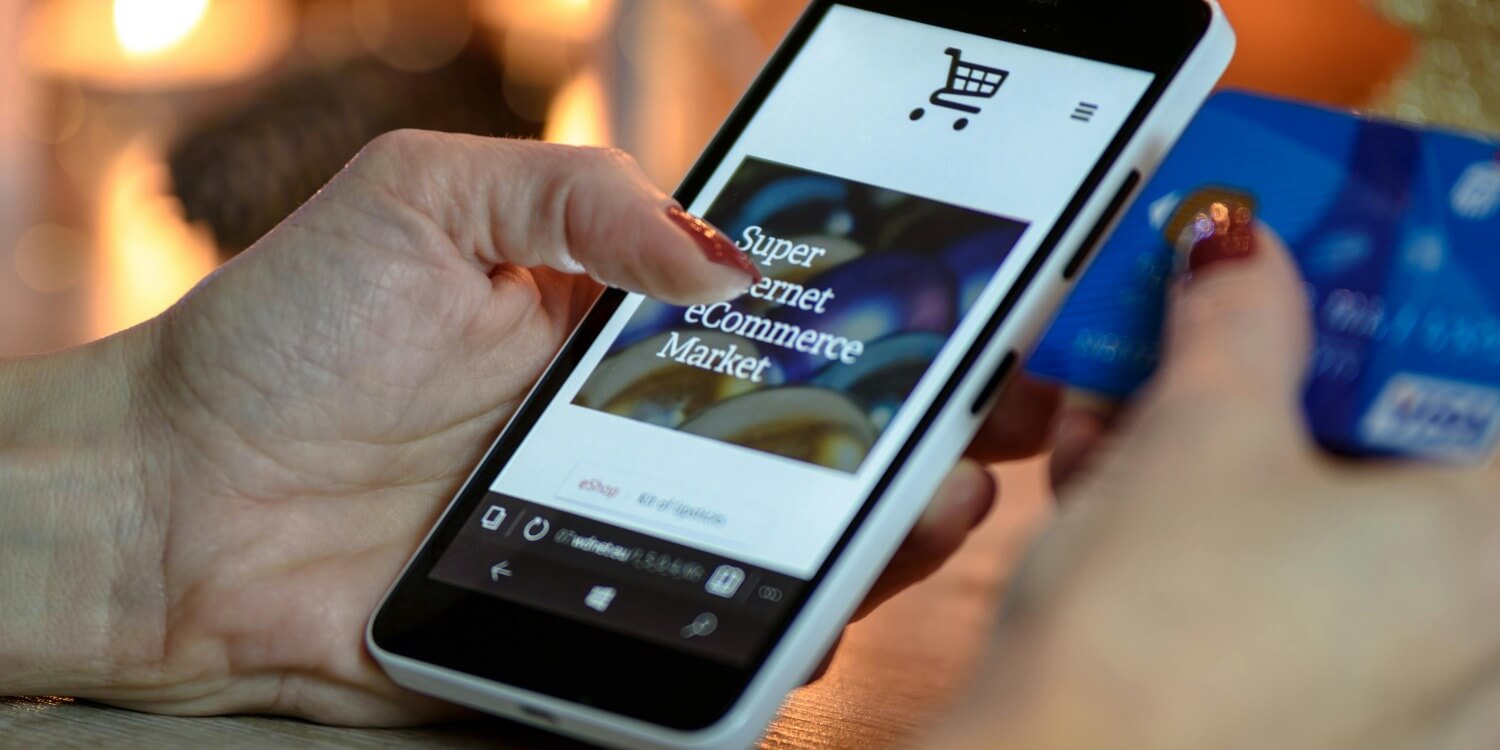 Personal online shopping through an ecommerce website on a smartphone, holding the smartphone in one hand and their card in the other.